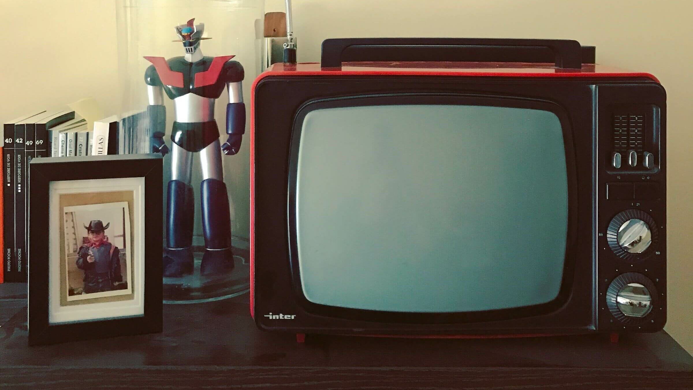 An old TV sits on a table next to a photo of a child and a robot toy